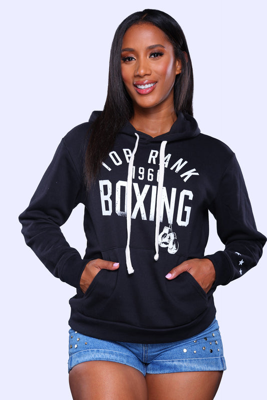 Person wearing a black pullover hoodie with "Top Rank Boxing 1966" printed in white on the front and three stars on the left sleeve, paired with black pants.