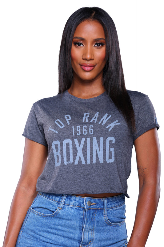 Woman wearing a charcoal crop t-shirt with "Top Rank Boxing 1966" printed in dark charcoal, paired with blue jeans.