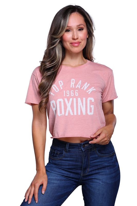 Woman wearing a desert pink crop t-shirt with "Top Rank Boxing 1966" printed in white, paired with blue jeans.