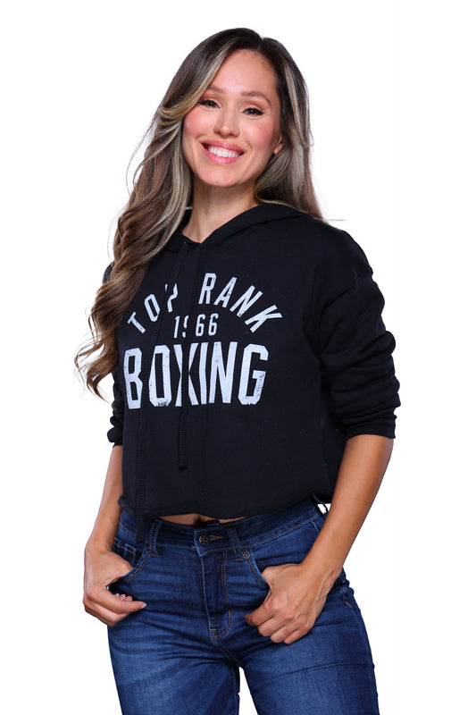 Woman wearing a black crop top hoodie with "Top Rank Boxing 1966" written in white, paired with blue jeans.